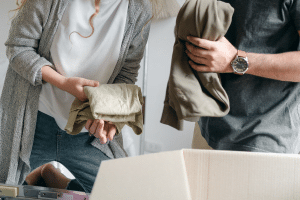 A man and a woman holding folded clothing, putting them in a cardboard box.