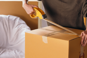 A woman taping the top of a medium sized cardboard box.