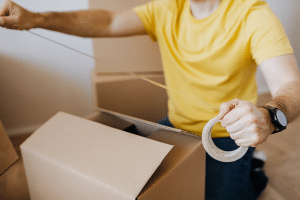 Man in yellow shirt taping up a cardboard box for his self storage facility unit.