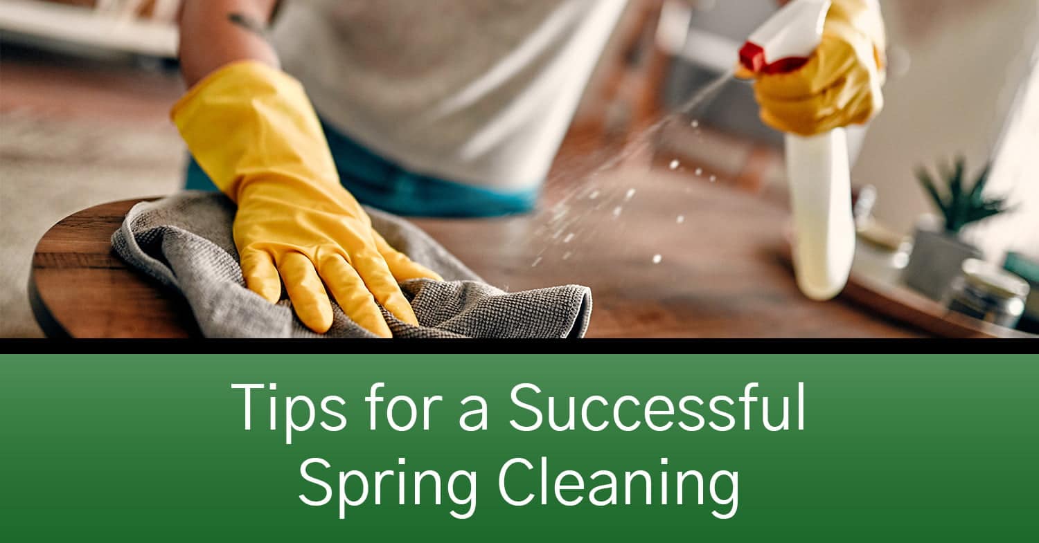 A person spring cleaning their home by wiping down a table in yellow rubber gloves.