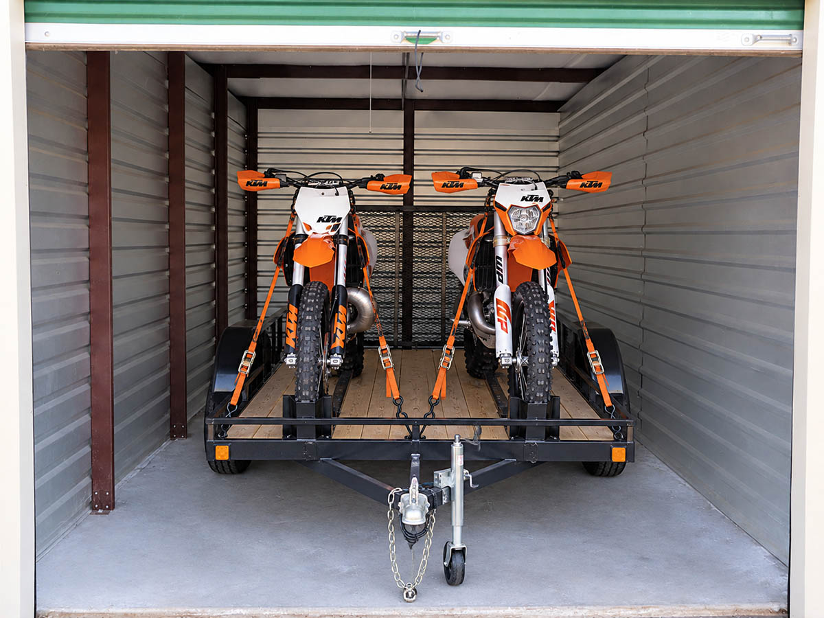 Dirt-bikes-and-trailer-storage-unit Dirt bikes strapped to a utility trailer inside an enclosed motorcycle storage unit in Wenatchee